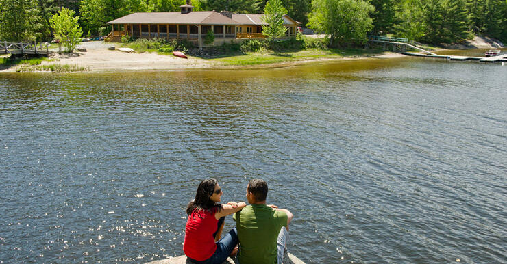 Man and woman sitting on rock looking at lodge on other side of river