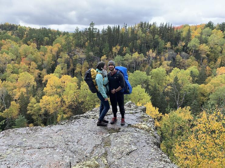 Man and woman with backpacks on standing on lookout over forest while backpacking in Ontario