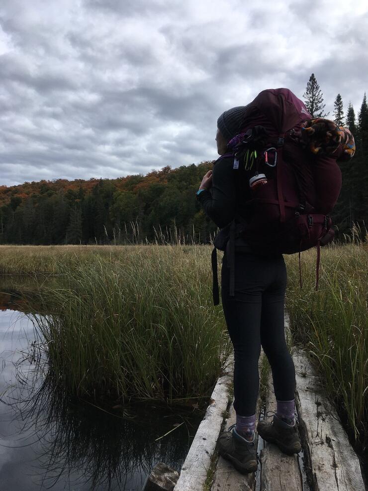 Woman with backpack standing on boardwalk over a marsh while backpacking in Ontario