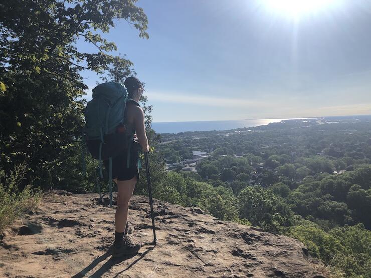 Woman with backpack standing at top of lookout over a city along the Bruce Trail