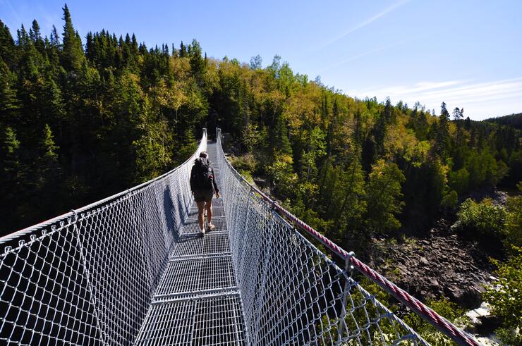 Person wearing backpack walking across suspension bridge