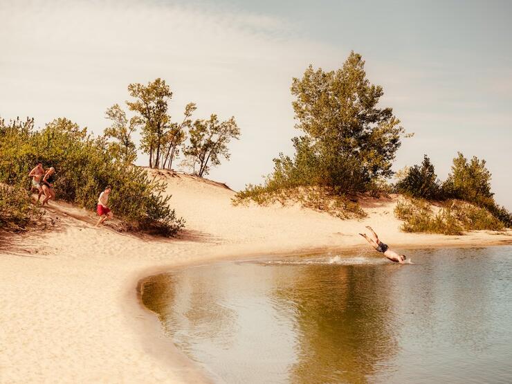 People running down sandbanks and jumping in the lake