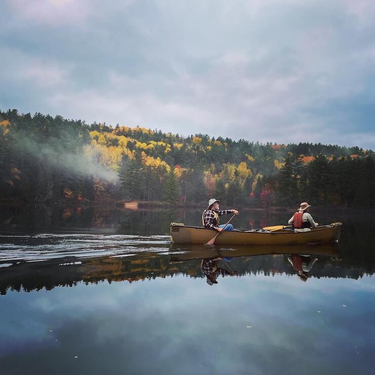 Two people paddling canoe with mist on the river and fall leaves in background during fall in ontario