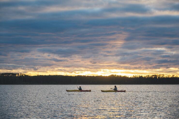 Two people paddling a kayak on a lake at sunset