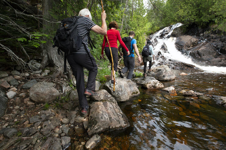 Four people hiking on rocks along stream leading up to waterfall.