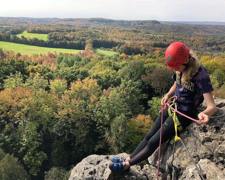 Woman sitting atop a cliff wearing rock climbing gear