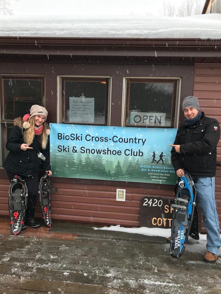 Man and woman standing with snowshoes on either side of BioSki sign