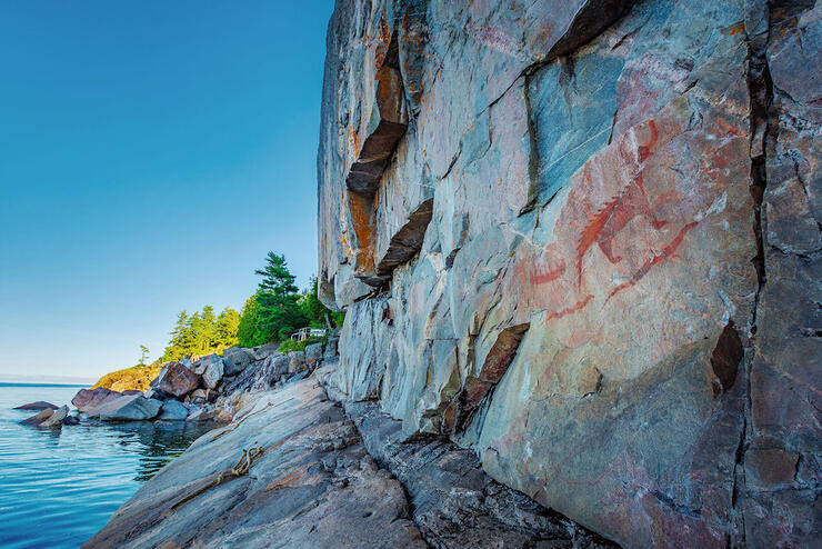 Pictographs on cliff face next to a lake.