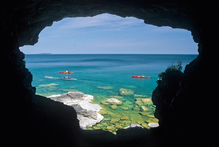 Looking out from a sea cave to people kayaking 