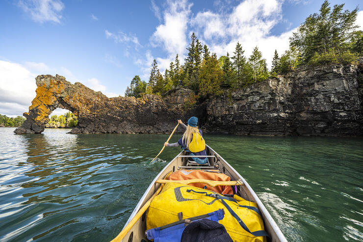Person canoeing towards a rock arch