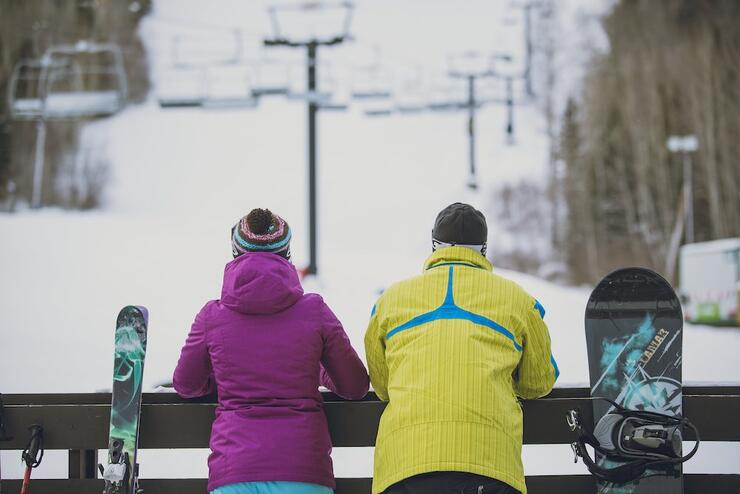 A skier and snowboarder standing at the bottom of the hill looking up at the lift