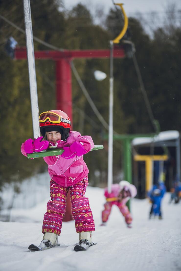 A little girl on skis riding a T-bar.