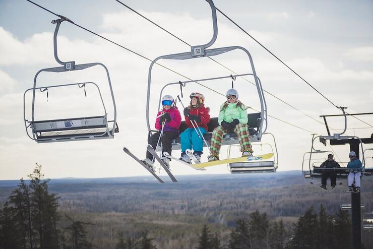 Three girls, two on skis and one on a snowboard, on a chairlift.