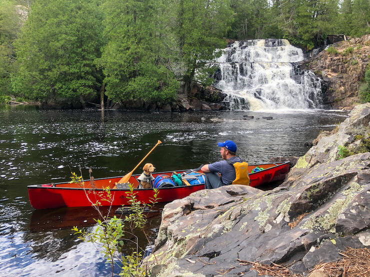 Man and dog sit in a canoe near a waterfall