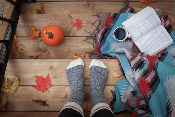 Looking down at sock feet on wooden stairs with coffee, blanket, book and pumpkin.