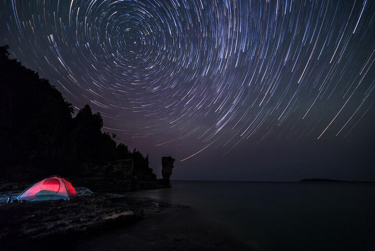 Stars overhead with tent lit up beside water