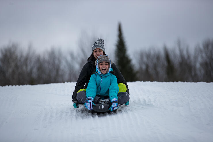 Mother and child on a sled going down a hill in the winter.