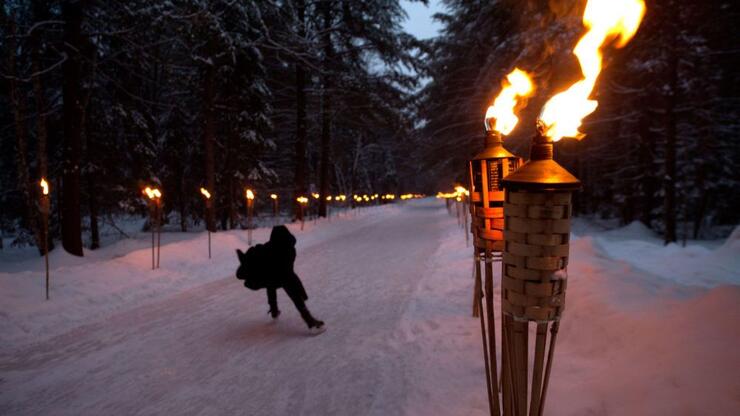 A person skates on a torch-lit ice trail
