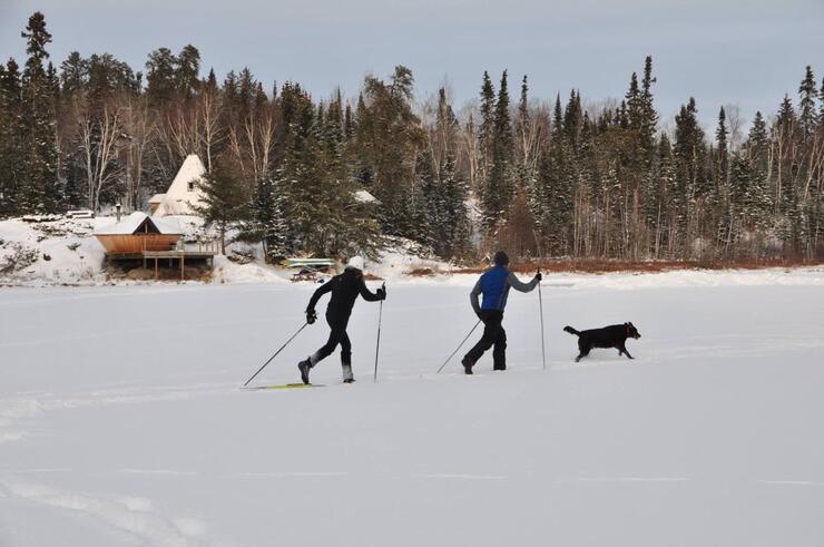 Two people ski across a frozen lake with their dog