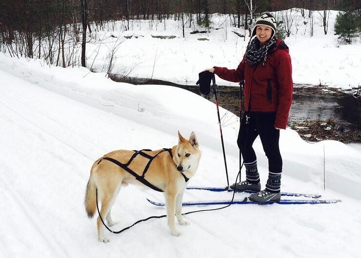 woman poses with dog while skijoring along winter trail