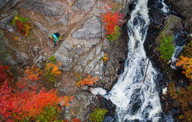 overhead view of a cyclist riding on rocky path beside a waterfall in Algoma Highlands
