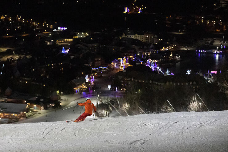 person skiing down Blue Mountain at night time with town lights in the background