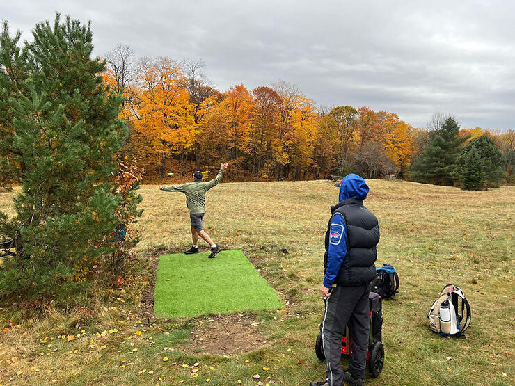 person throws a frisbee at disc golf course in fall