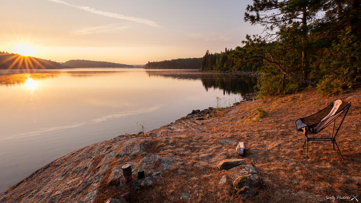 Camp chair waiting on shore at sunset.