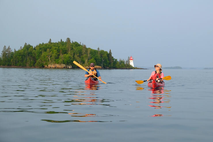 Two people paddling with lighthouse in the background