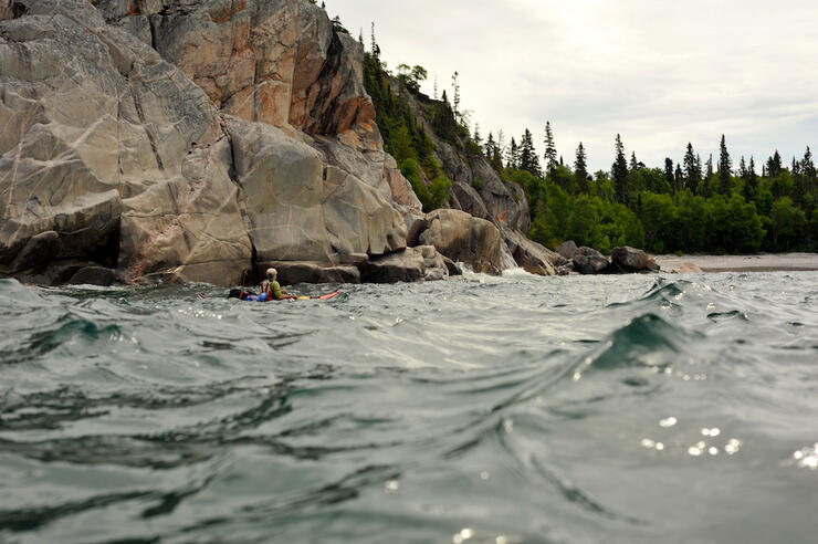 person paddling kayak with rock cliff in background