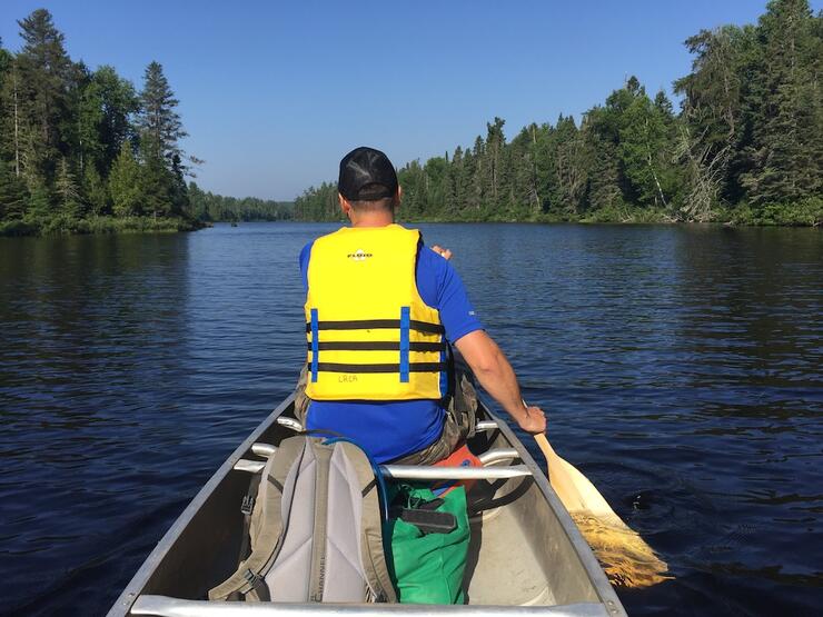 Bow shot of a man paddling a canoe through a backcountry lake