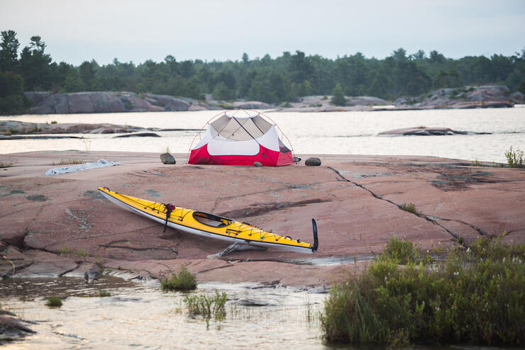 Yellow kayak and red tent on rocky ground.