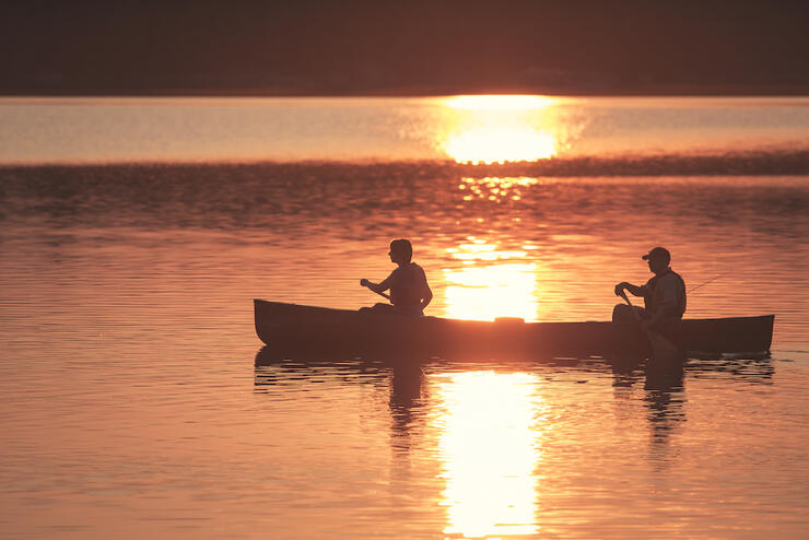 Two people paddle canoe at sunset.