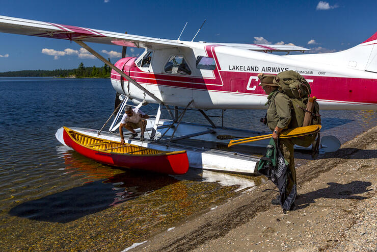 Man carrying pack to float plane with canoe alongside.