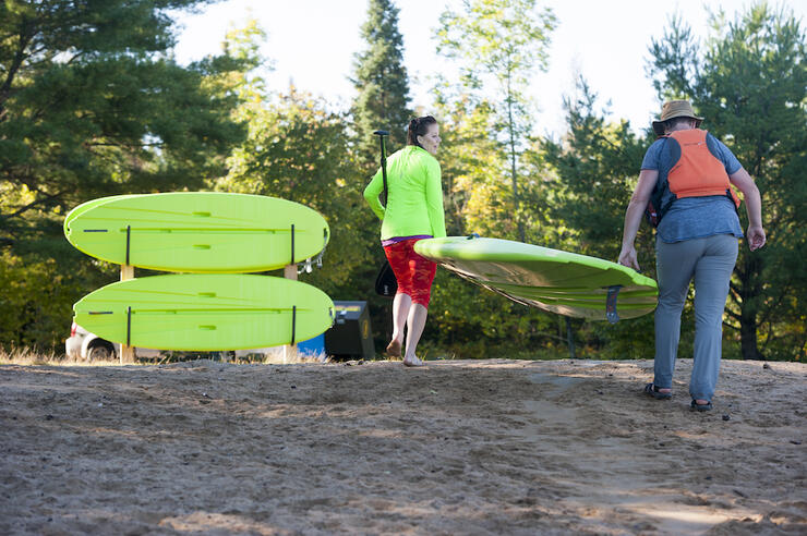 Two peopling carrying a green paddleboard 