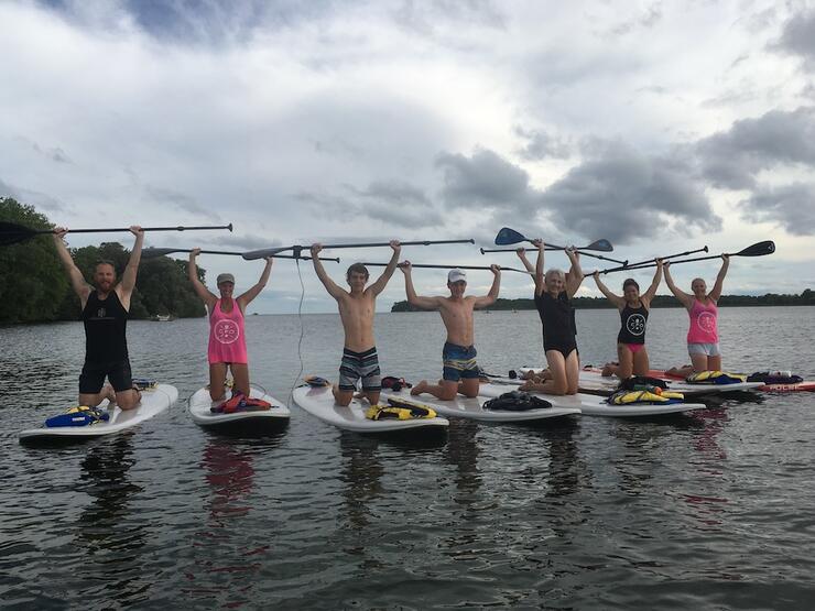 Group of people on sup with arms raised holding paddle in the air over their heads