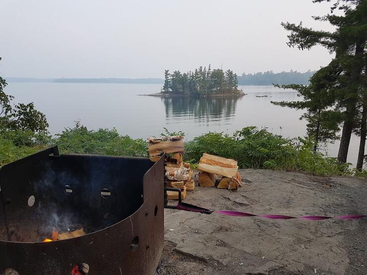Looking out over lake with fire ring and campfire wood in foreground.