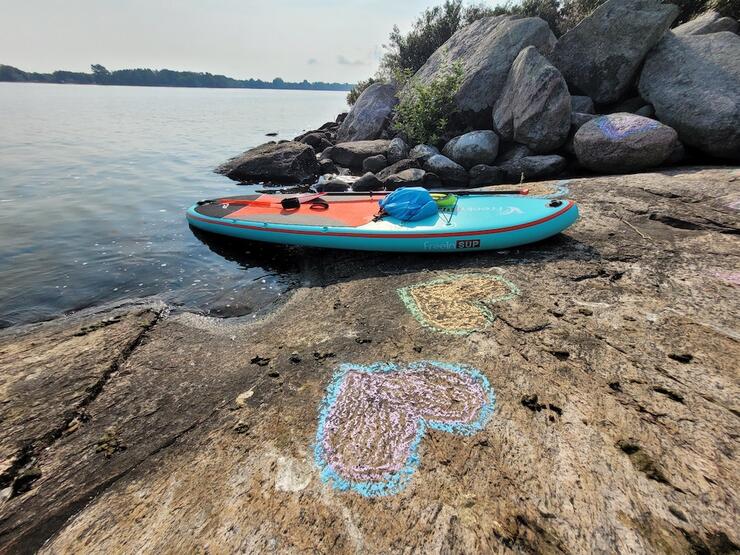 Paddleboard beached on a rocky lakeside shelf with a large chalk heart drawn on the rocks