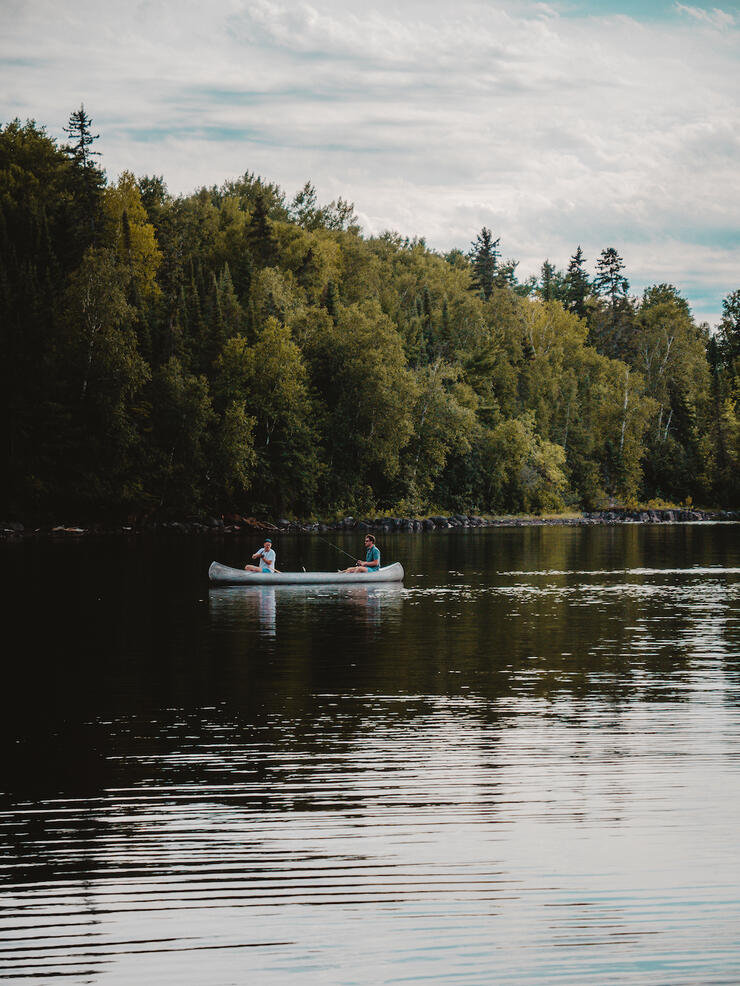 Two people fishing from aluminum canoe.
