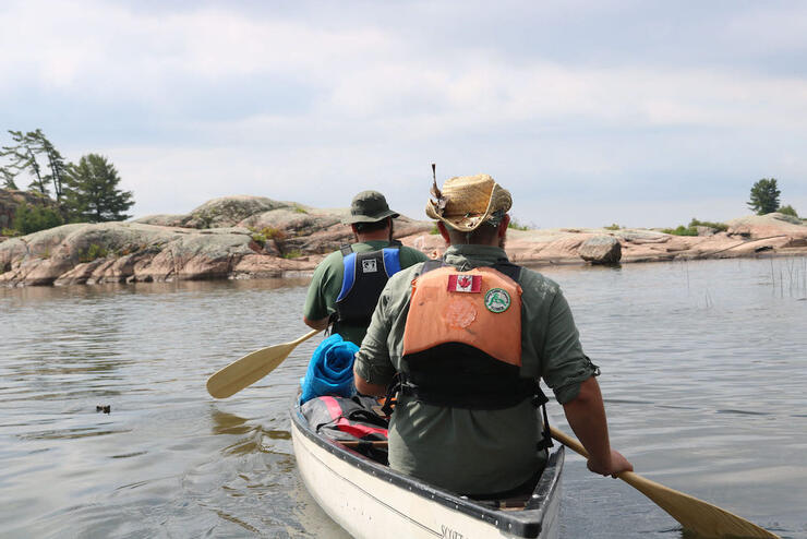 Two men paddling a white canoe toward a rocky shoreline.
