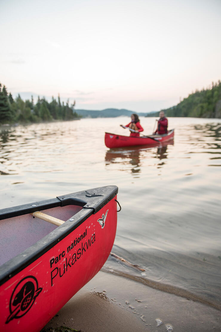 A couple paddles a red Parks Canada canoe at sunset.