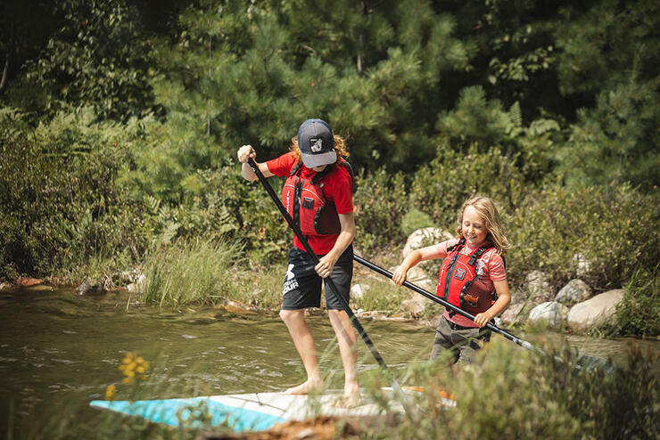 two kids standup paddleboarding together at Kivi Park in Sudbury