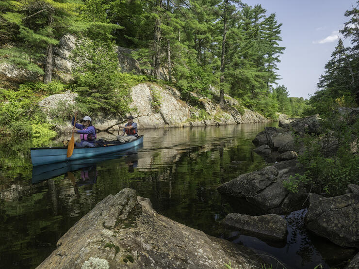 Couple paddles green canoe through narrow passage between rocks.