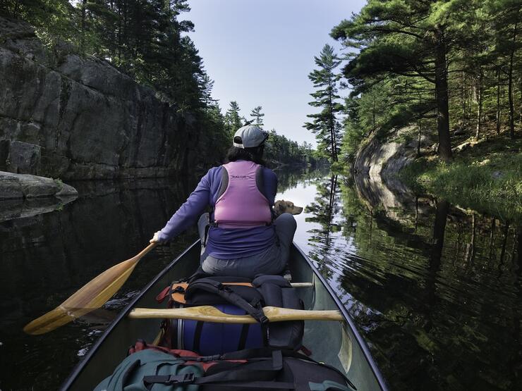 View from stern of canoe of female paddler and dog in the bow.