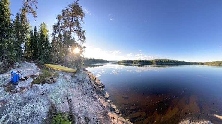 Sunrise next to rocky campsite with yellow canoe overturned.