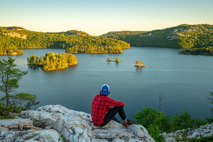 Man wearing flannel sitting atop rocky lookout over lake.