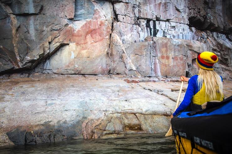 Woman in bow of canoe looking at pictographs.