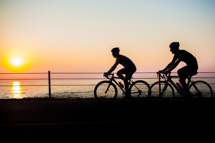 Two cyclists riding beside a lake at sunset
