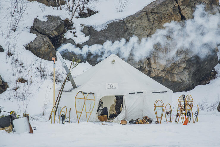 Large white canvas tent with smoke coming out of a stove pipe, surrounded by snow.