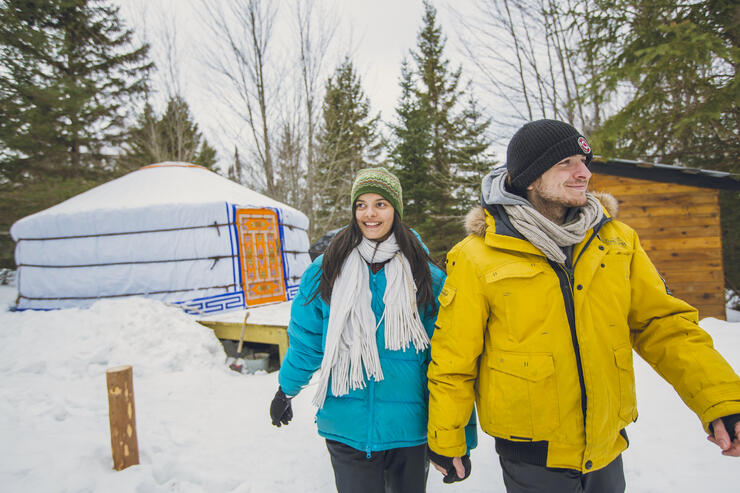 A couple walking in front of a Mongolian yurt in the winter.